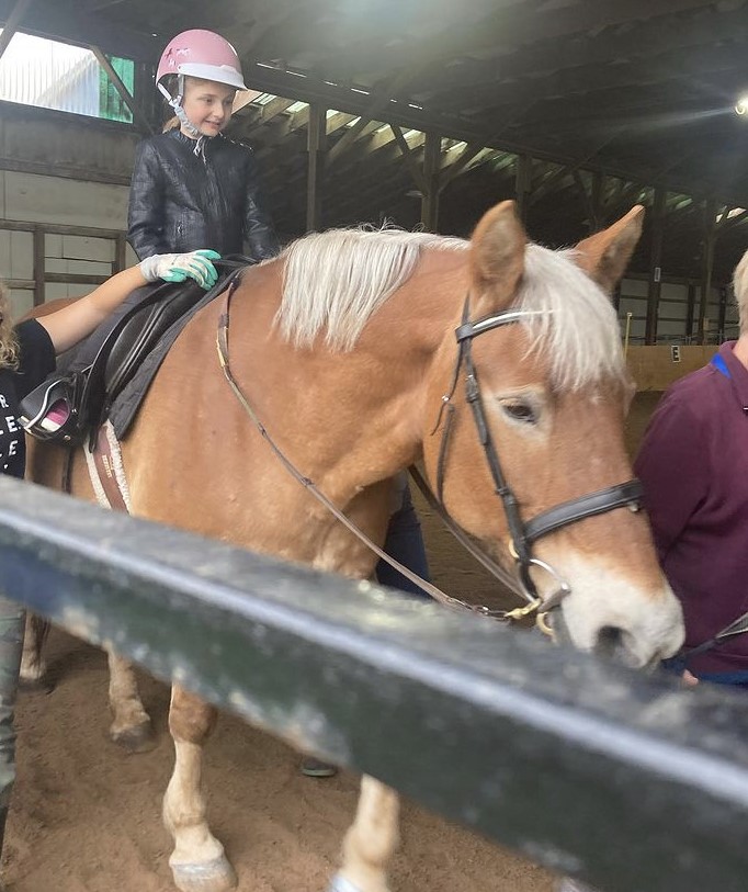 A young rider in her lesson riding Lexie, with two volunteers side walking beside her. 