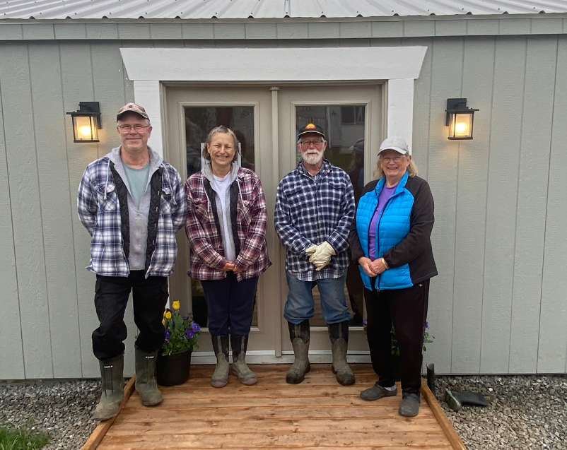 Four volunteers standing together with big smiles in front of the clubhouse