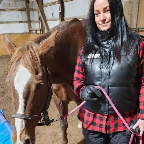 A woman in a black vest and red plaid shirt holding onto Lady with a lead rope in our indoor arena.